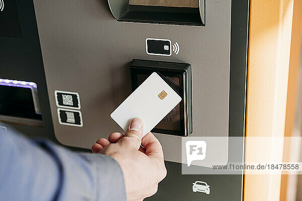 Hand eines Geschäftsmannes mit Kreditkarte am Fahrkartenautomaten