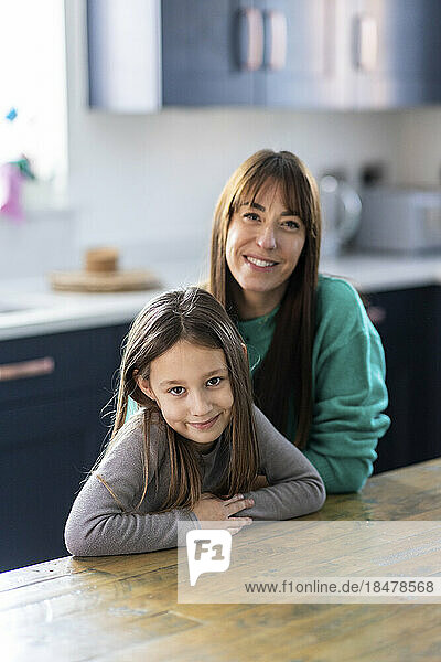 Happy mother and daughter sitting at table in home