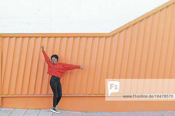 Glückliche Frau mit erhobener Hand steht vor einer orangefarbenen Wand