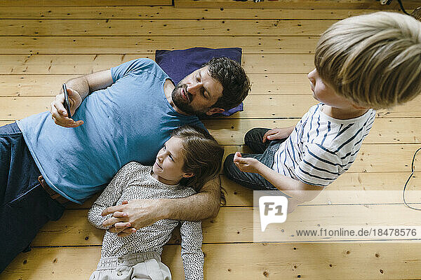 Vater teilt Smartphone mit Tochter und Sohn  die zu Hause auf dem Boden liegen
