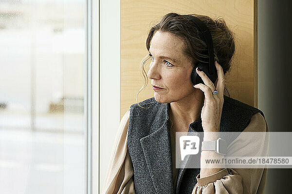 Woman adjusting wireless headphones by window
