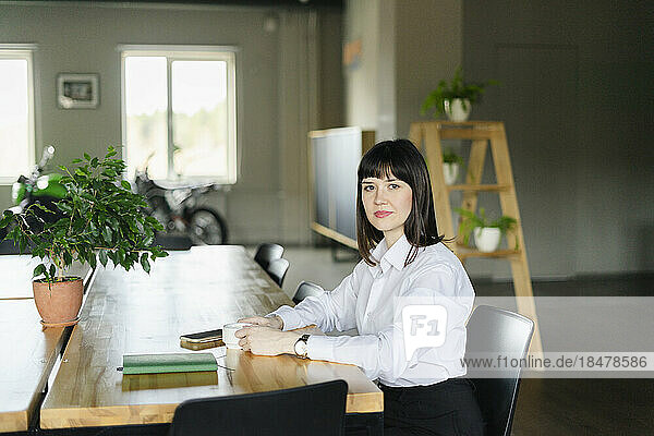Portrait of confident brunette businesswoman sitting at table in office
