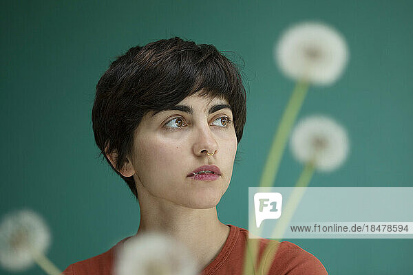 Contemplative woman with dandelions against green background