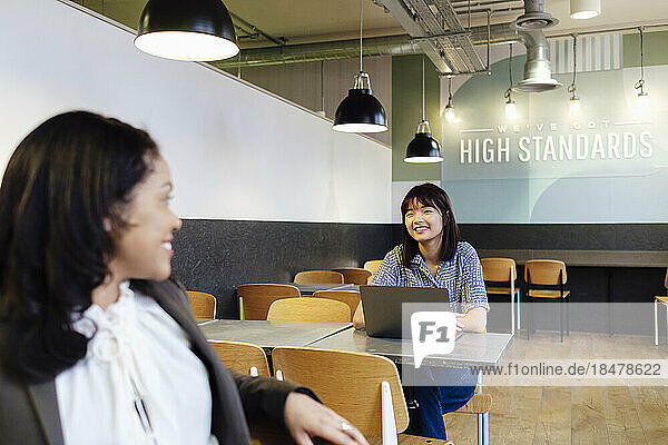 Smiling businesswoman talking to colleague sitting at office cafeteria
