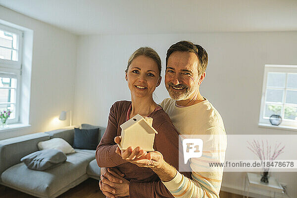 Smiling couple holding house model at home