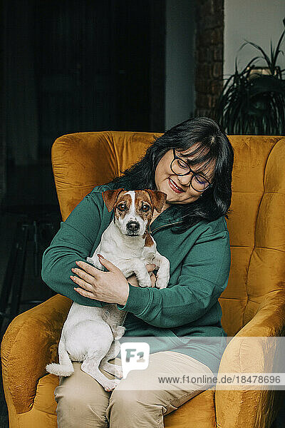 Happy mature woman sitting with dog on armchair