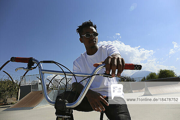 Man wearing sunglasses sitting on BMX bike at skatepark