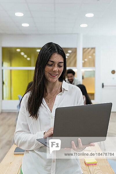 Geschäftsfrau benutzt Laptop im Büro mit Kollegen im Hintergrund