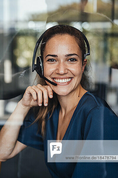 Happy businesswoman wearing headset sitting in soundproof cabin