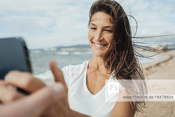Happy woman taking selfie through mobile phone at beach