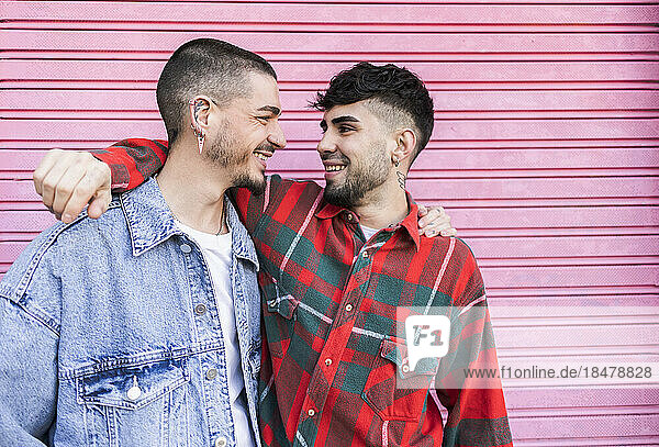 Happy gay couple with arms around standing in front of roller shutter wall