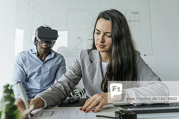 Architect preparing blueprint with colleague wearing virtual reality headset at office