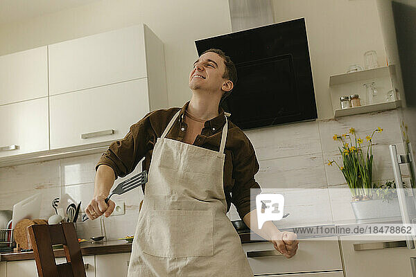 Happy man wearing apron dancing in kitchen at home