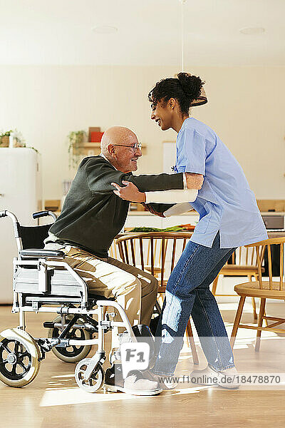 Heimpfleger hilft älterem Mann beim Aufstehen aus dem Rollstuhl