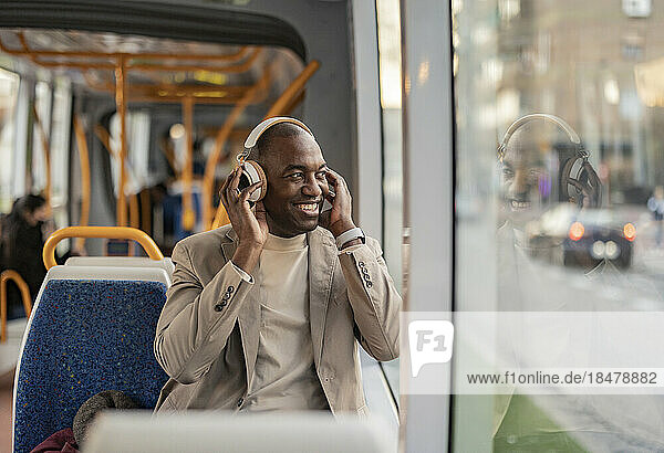 Happy commuter wearing wireless headphones and looking out of window in tram