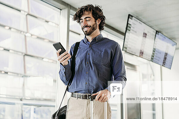 Smiling young businessman using mobile phone at station