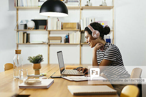 Geschäftsfrau trägt Kopfhörer und benutzt Laptop am Tisch