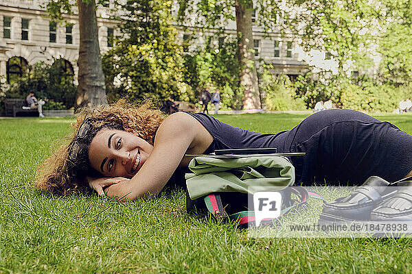 Lächelnde junge Geschäftsfrau  die im Park auf Gras liegt