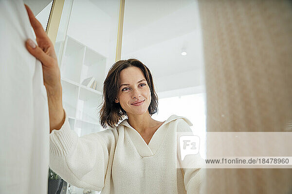 Smiling woman choosing clothes from closet at home