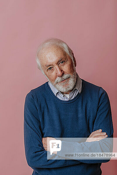 Elderly man with arms crossed against pink background