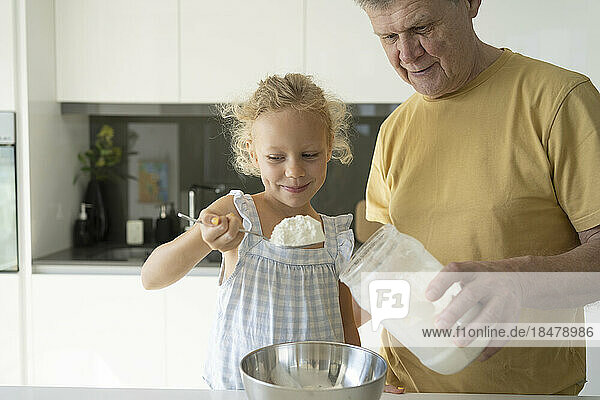 Smiling girl holding flour in spoon by grandfather at home