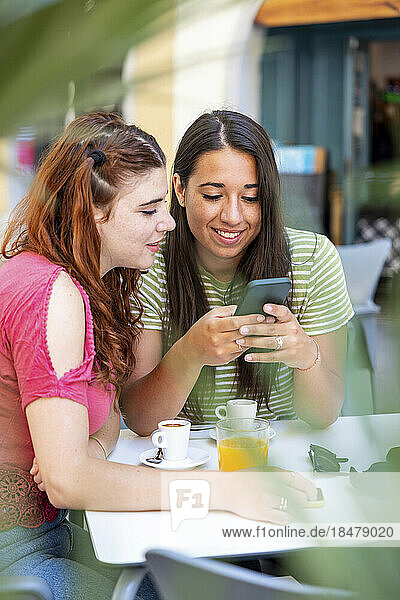 Woman sharing smart phone with girlfriend in sidewalk cafe
