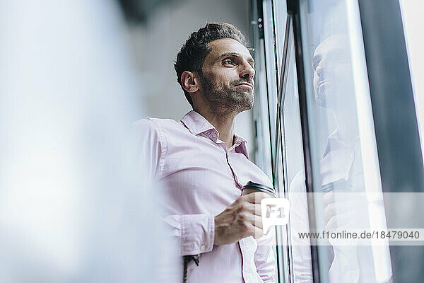 Nachdenklicher reifer Geschäftsmann mit Kaffeetasse  der durch das Fenster schaut
