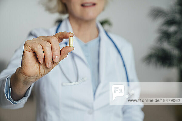 Mature doctor showing capsule pill at clinic
