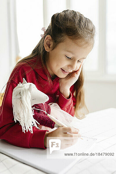Cute girl with toy doing homework at home