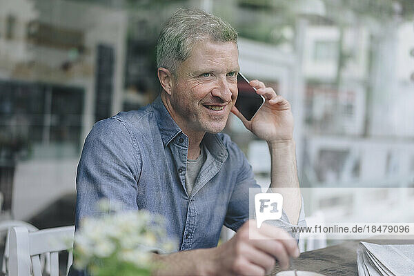 Happy man talking on mobile phone seen through glass