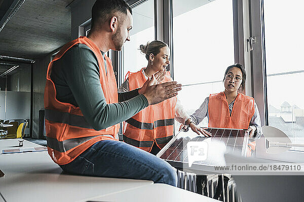 Multiracial colleagues wearing reflective clothing discussing over solar panel at office