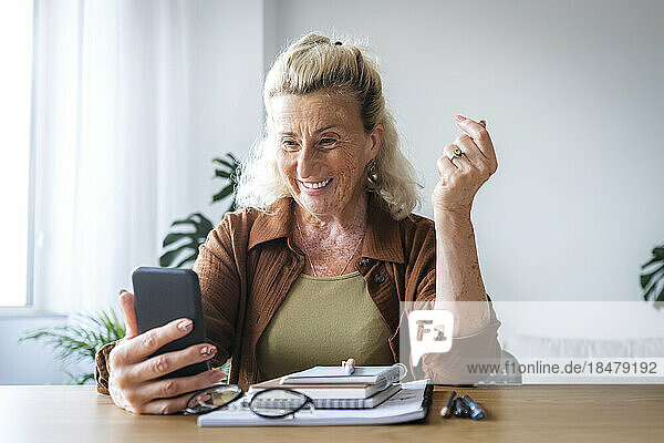 Happy senior businesswoman holding mobile phone at desk in home office