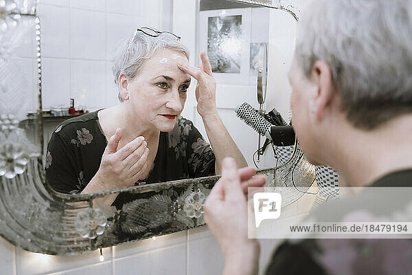 Spiegelbild einer älteren Frau  die im Badezimmer Gesichtscreme aufträgt