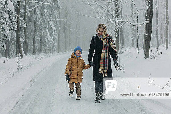 Mother walking with son on road in snowy forest