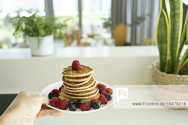 Hand holding stack of fresh pancakes on plate at home
