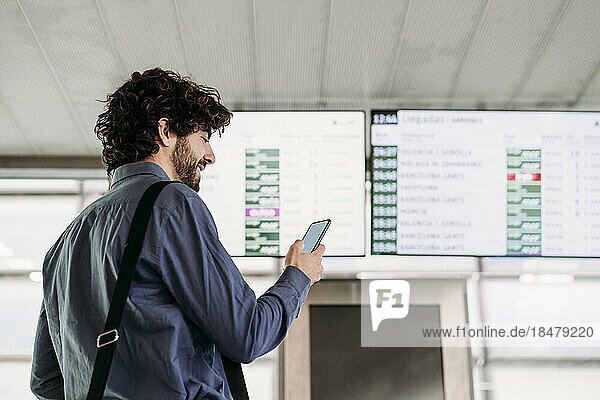 Businessman using mobile phone in front of arrival departure board