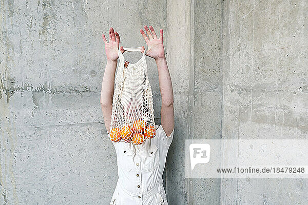 Non-binary person with bag of oranges in front of wall