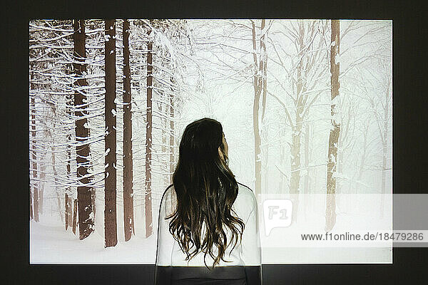 Woman looking at snowy forest projection on wall