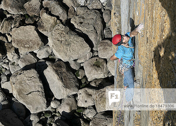 Sportsman climbing rocky wall on sunny day