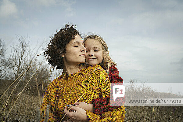 Smiling girl hugging mother from behind in front of sky