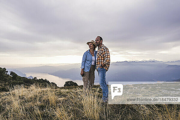Mature couple standing together on mountain at sunset