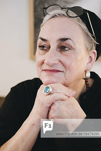 Thoughtful senior woman with hand on chin at home