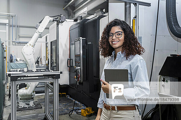 Happy young engineer standing with tablet PC in front of machine