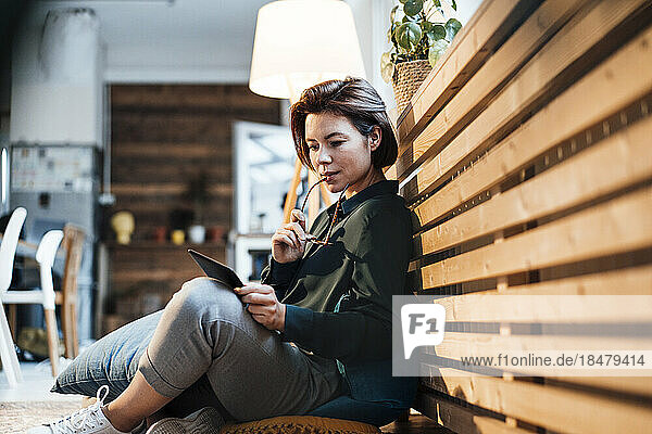 Young businesswoman with tablet PC sitting by heating radiator in office