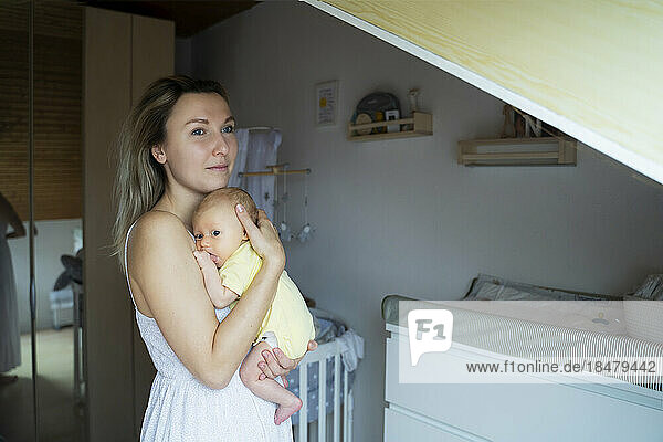 Contemplative mother with baby boy standing at home
