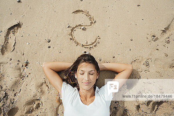Frau mit geschlossenen Augen schläft im Sand am Strand