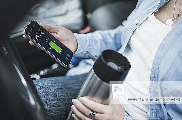 Mature woman with thermos flask using electric car charging app