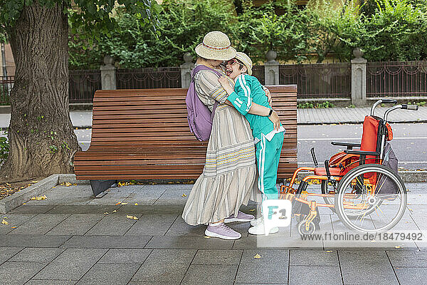 Mother embracing daughter with disability standing near bench