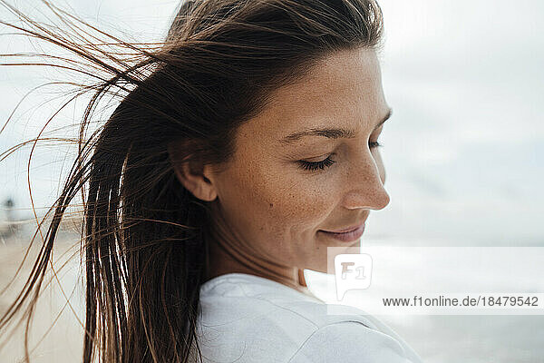 Lächelnde brünette Frau mit geschlossenen Augen verbringt ihre Freizeit am Strand