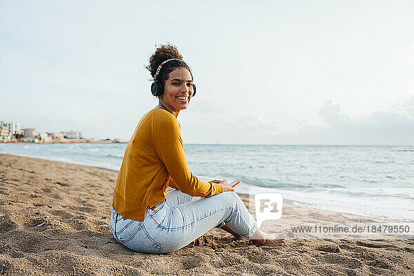 Glückliche Frau mit kabellosen Kopfhörern  die am Strand Musik hört